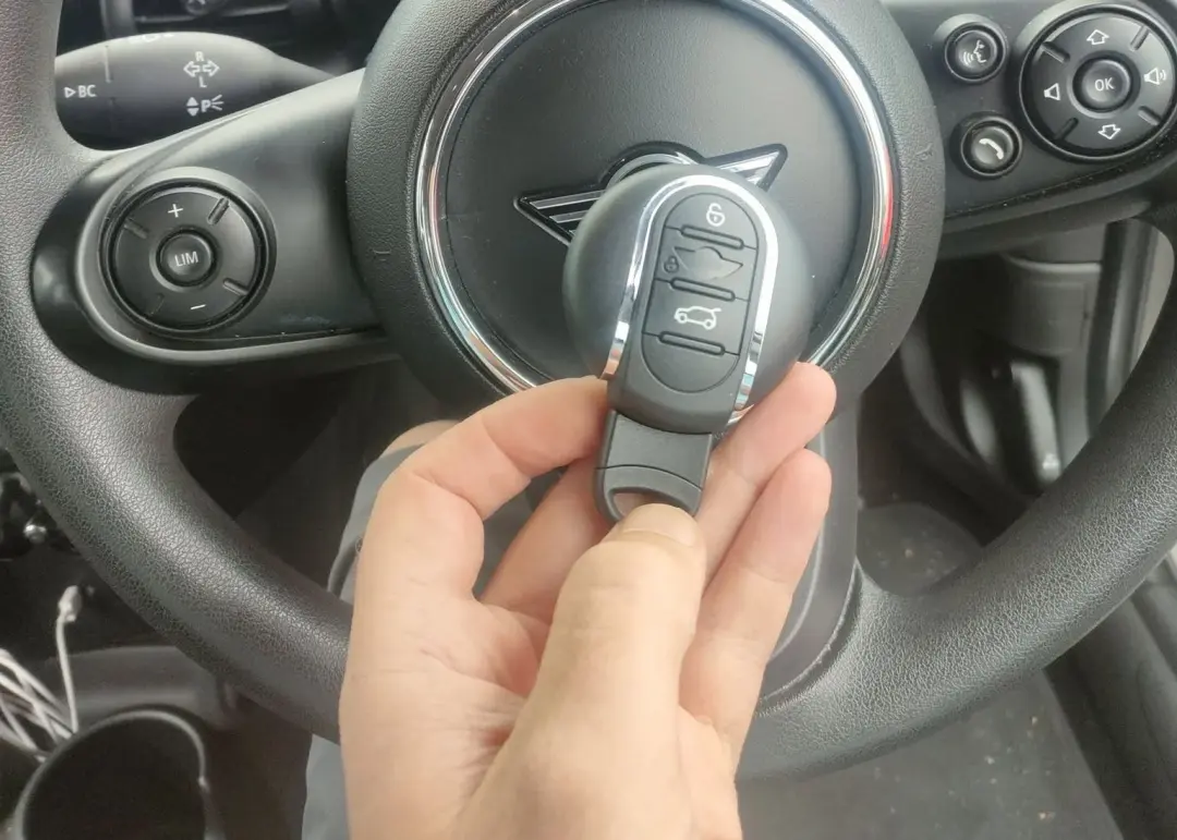 Hand holding an oval remote key beside a round vehicle dashboard