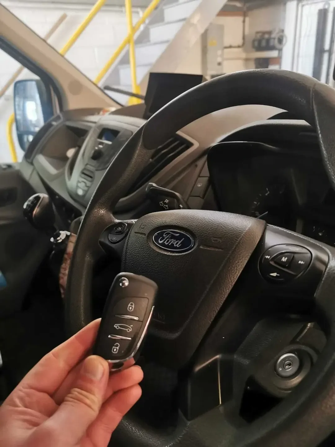 Hand holding a flip key inside a vehicle in a workshop