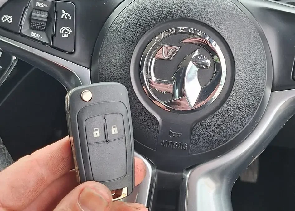 Hand holding a remote key in front of a vehicle instrument cluster