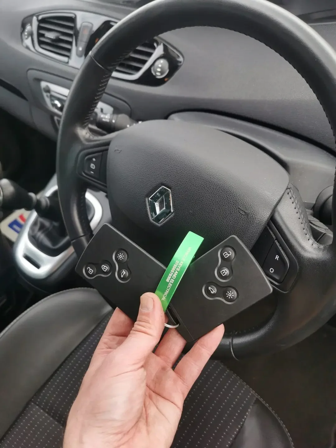 Hand holding two vehicle key cards beside a steering wheel