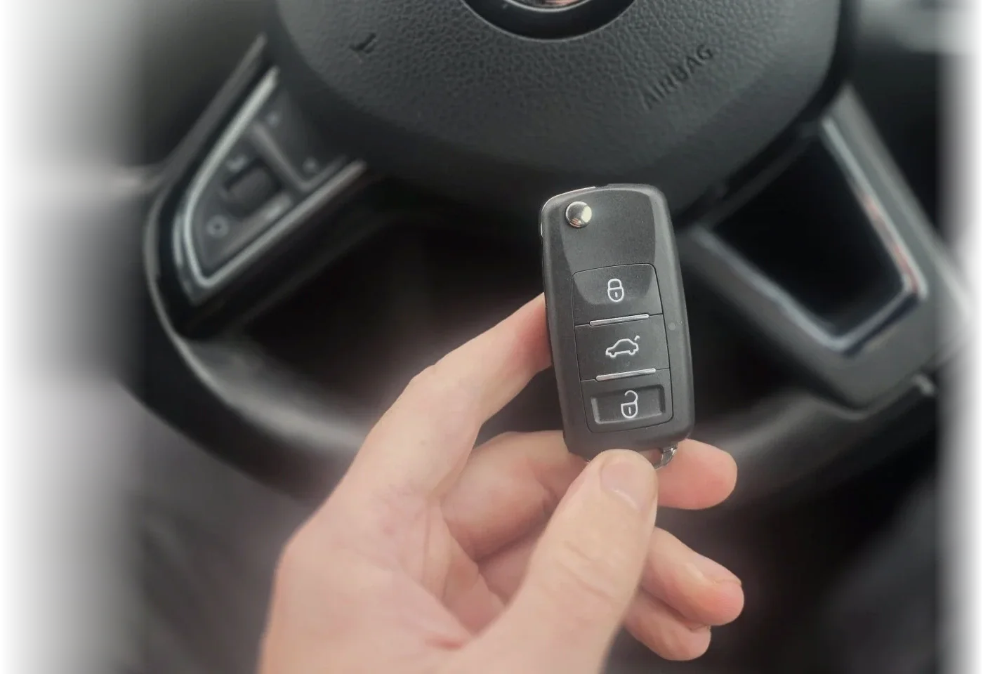 Hand holding a three-button remote key beside a grey steering wheel