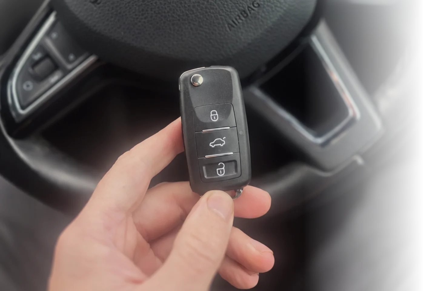 Hand holding a three-button remote key beside a steering wheel
